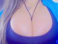 Les seins volumineux et ronds de GilliSkquirtty sont mis en valeur par un haut noir moulant, laissant entrevoir une grande partie de sa poitrine, avec un collier au centre. Ses longs cheveux bruns sont sur la gauche..