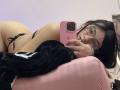EvaaFarix lying on pink chair, wearing black string bikini, glasses, holding pink iPhone, black hoodie, looking at mirror, butt up, hand on head, bracelet on wrist, black hair.