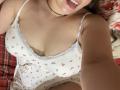 Madrinia's tits are visible in a white, floral, lace-trimmed, low-cut camisole. She's sticking out her tongue, with a black choker and blonde hair. Her arm is in the shot.