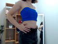 Steisii with blue strapless top, showing slim waist and black leather pants, hand on hip, reflection in mirror, light brown hair, no visible tits or pussy.