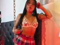 CataMoreno with long black hair, wearing a sheer pink bra with white frills, exposing her small tits, and a red plaid skirt, standing near a chain.