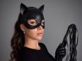 AmmaLoyXX with cat mask, holding black leather flogger, wearing black shirt and earrings, has wavy brown hair, looking confident, has small tits, and is holding flogger in right hand.