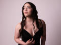 AnnFisher with wavy dark hair, wearing a low-cut black dress, exposing her tits, looking to the side, holding the dress, light skin, subtle makeup, small necklace.