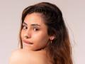 AntonellaReed has long brown hair, a nose ring, and is looking over her shoulder with a subtle smile, showing her bare shoulder and small gold earrings.