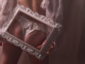 RosaVance's ass, wearing white ruffled panties, holds an ornate white frame against her back. She's in a lace robe, with her hands on the frame's edges.