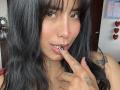 ElizabethMacy with black hair, nose ring, tattoos on fingers, and tongue touching black nail, looking at camera with slight smile, showing her pink lips and cute face.