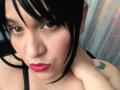VivianaThompson has black hair, pink lipstick, and a butterfly tattoo on her shoulder. Her hand touches her neck. She has a pinkish blush on her cheeks.