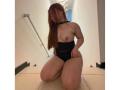 VicluX kneeling on tile floor, wearing black high-cut bottoms, topless with small tits, long red hair covering face, hands on hips, in a dimly lit, narrow hallway.