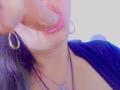 GilliSkquirtty's glossy lips are wrapped around a thick, circumcised cock, with her gold hoop earrings and butterfly necklace visible, wearing a black top, in a slightly blurry photo.