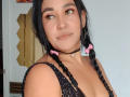 EdenIvyLm a des tresses noires avec des rubans roses, un anneau au nez et un anneau aux lèvres, elle porte un collier noir et un haut scintillant, avec des yeux verts et un sourire discret..