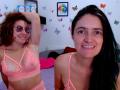 LunaVenus with curly brown hair, glasses, and pink lace bra, showing tits, smiling. Another LunaVenus with black hair, pink lace bra, and visible pussy, smiling. Bedroom.
