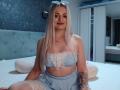 CoquineElise has long blonde hair, wears a blue checkered lingerie set with lace, showing her tits and a tattoo on her right arm, sitting on a bed.