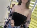Nesie with bare shoulders, black strapless top, pink plaid shirt off, blue jeans, butterfly decor, tiger toy, necklace, blonde hair, partial face, hands on jeans.
