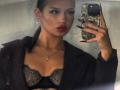 ShanekaKonig with dark hair in a ponytail, red lipstick, black lace bra, and dark jacket, holding a phone with a floral case, showing off her tits.