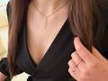 Kattina's chest with a black V-neck shirt, gold cross necklace, and a ring on her right hand, showing purple-painted nails, her brown hair on both sides.