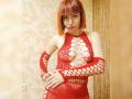 LaylaHottyX with red bob, wearing a red mesh dress with large cutouts, exposing her tits, and matching arm sleeves, standing in a room with beige walls.