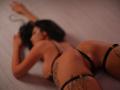 SalmaJade è sdraiata a pancia in giù, indossa un intimo nero con spalline sottili, e ha dei tatuaggi sulla coscia e sui glutei. Il suo sedere è ben visibile, con le braccia allungate sopra la testa..