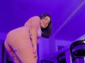 SherylHill in pink lingerie, bending over with a smile, showing her ass and a pink dildo in her pussy. Purple room, black bar stools, mirror in background.