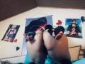 CristalZafiro's ass is up, wearing black high heels, with feet in the air, showing soles, in a bedroom with anime posters and a blue flag on the wall.