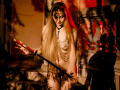 MiaMeowa with long blonde hair, naked, wearing chains and a nose ring, holding a katana, standing in a dimly lit, red-hued room, shadow on her tits.