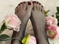MiraRosse's feet in black fishnet stockings, toes painted dark red, resting on white fluff with pink roses, green leaves, and a yellow rose at the bottom.