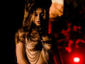 MiaMeowa with long brown hair, wearing a chain-covered top that exposes her tits, standing in dark, red-lit background, looking down with closed eyes, shadow on her face.