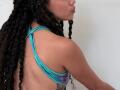 TerryGreen with long, curly black hair, wearing a blue and purple halter top, showing her bare back and a tattoo on her left side, pouty pink lips.