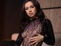 IsadoraReyes with long dark hair, wearing a sheer black lace top, exposing her small tits, and covering her right hand over her chest. Soft, confident expression.