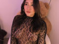 ElyRoss has dark lace over her tits, wearing a see-through black top, with long brown hair, hoop earrings, and a small nose ring, sitting in front of a big teddy.