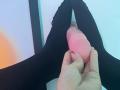 La main d'IrisBlair tenant un sextoy réaliste rose entre ses jambes noires écartées. Ses doigts, avec du vernis à ongles rose, agrippent le sextoy près de son pénis rasé, érigé et non circoncis..