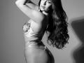 FerAram with long wavy hair, wearing shiny satin lingerie, has curvy ass, small tits, and a sexy side profile, arms raised, black and white, high-contrast, sensual.