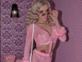 MademoiselleBella with blonde curls, wearing pink, sheer, tied-up, furry long-sleeve top, exposing her big tits and pink lace bra, holding pink sunglasses, with a pink tattoo on her side.
