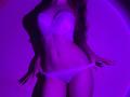FlyFreedom with white lace bra and panties, purple-lit, showing off her tits and pussy, hands on her panties, long wavy hair, slim and sexy, confident pose.