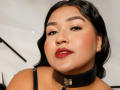 DojaAissha has a dark collar with a metal ring, full red lips, and black eyeliner, with black hair and a confident expression, showing her shiny ass.