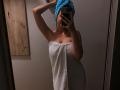 Olieri with a blue towel on her head, holding a phone, covering her face, wearing a white towel that barely covers her tits and ass, in a mirror selfie.