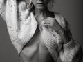 EolantaMarina with her tits partially exposed, wearing a knitted sweater, her hand pulling it down, revealing her ribcage, in a black-and-white, intimate, minimalist photograph.