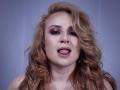 ScarlettCaarter a les cheveux blonds bouclés, des yeux brun-rosés avec un maquillage prononcé, et elle tire légèrement sa langue, qui est un peu visible. Elle porte un collier en argent..