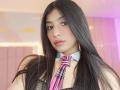 NaiaSanders with long black hair, pink and purple striped necktie, white collar, black mesh top, nose ring, and pink lips, looking at camera. Soft pink lighting.