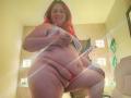 RouseWright with red hair, smiling, wearing a grey top lifted to expose her big tits, and red panties, showing her fat belly and ass, standing in a room.