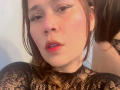 SophiaQueens with red lips, black lace top, and nose ring, looking slightly annoyed. Her wavy brown hair is partially over her shoulder, and her makeup is bold.
