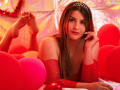 SaraWestt with long brown hair, red sparkly dress, and tiara, lying on red balloons, her cute face, small tits, and hand on cheek, surrounded by red decorations.