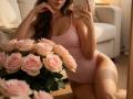 Diantrisy with pink tank top, showing tits in mirror selfie, pink roses in foreground, knee on carpet, phone in hand, long brown hair, soft lighting, cozy room.