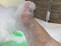 EliseMonet's foot, covered in white bubble foam, is raised in a green-tinted bath. Her pinkish skin is visible through the soap. The image is a high-resolution shot.
