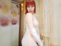 LaylaHottyX with red bob, white lace bodysuit, and cutout sleeves, showing her tits and ass, standing by a window with fairy lights.