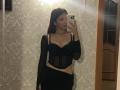 ElbaHuppenbauer with small tits, wearing a black sheer top and black skirt, taking a mirror selfie, holding an iPhone, in a room with ornate wallpaper.