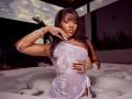 LennyRosses, dark-skinned, with wet white shirt, covering her big, wet boobs, and soapy hands, in a hot tub, against a twilight sky, with a pearl necklace.