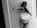 Black-and-white selfie of Olieri with long dark hair, wearing a white crop top and strappy black panties, holding a phone covering her face, showing her tits and pussy.