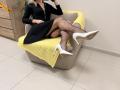 Rorria, avec des bas résille, des talons hauts blancs, une robe noire et une couverture jaune, assise sur une chaise grise, tenant un téléphone, montrant ses fesses..
