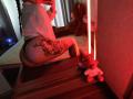 Niferttiti with a large floral tattoo on her thigh, wearing black panties and a white shirt, sitting on a wooden dresser, taking a mirror selfie with red lighting.