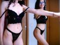 SweetClaraa in black lace lingerie, showing her tits and pussy in a mirror, with curly hair and glasses, smiling, adjusting her strap, in a wooden room.